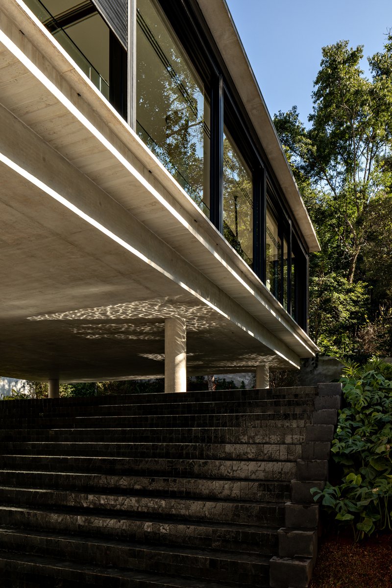 Dark stone staircase ascending beneath a cantilevered concrete soffit with recessed linear lighting at midday