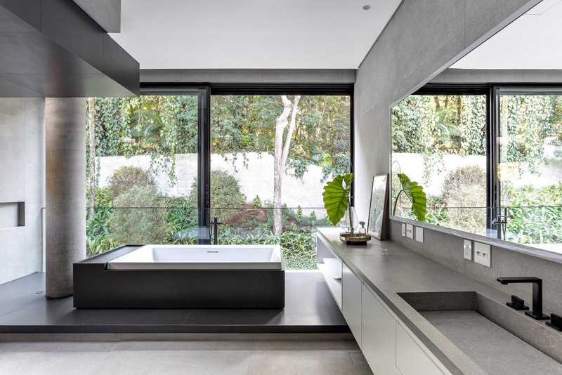 Freestanding bathtub on a black plinth framed by windows opening to a landscaped garden