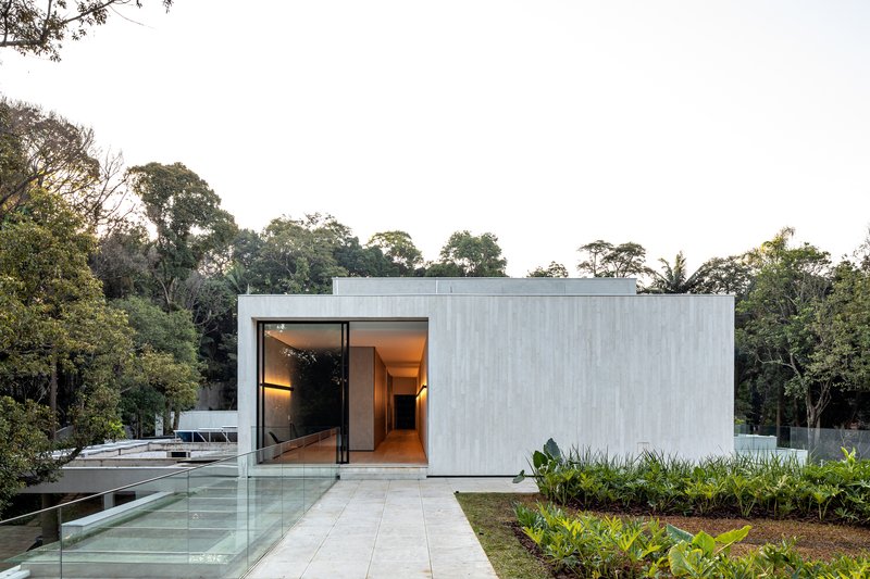 Rectilinear concrete volume with large glass opening approached by a stone-paved pathway flanked by planted beds