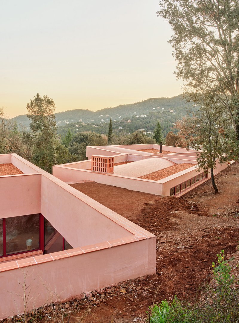 Rooftop view of the pink stucco volumes with gravel-filled terraces and brick chimney at dusk