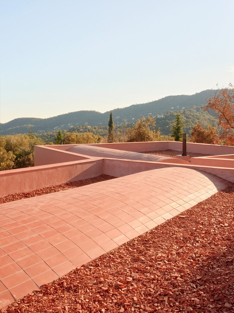 Rooftop terrace with curved tile paving, crushed stone beds and hillside views in morning light