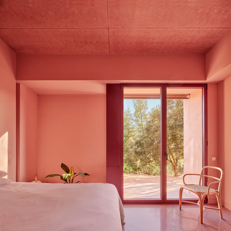Bedroom with pink stucco walls, sliding glass doors to garden, and bentwood chair beside the bed