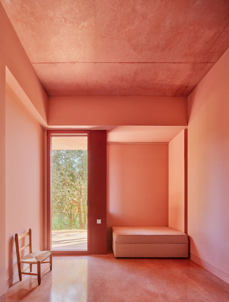 Bedroom with tall window framing trees outside and built-in bed niche in pink plaster