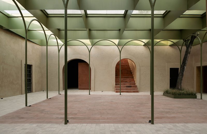 Skylit courtyard with arched steel colonnade framing arched doorways and a brick staircase