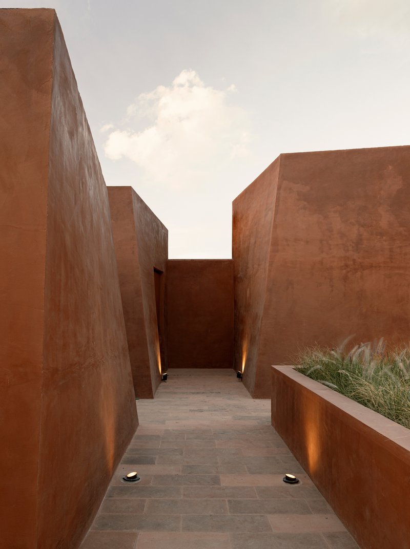 Passageway between corten steel walls with planted bed and uplighting beneath a white cloud-filled sky