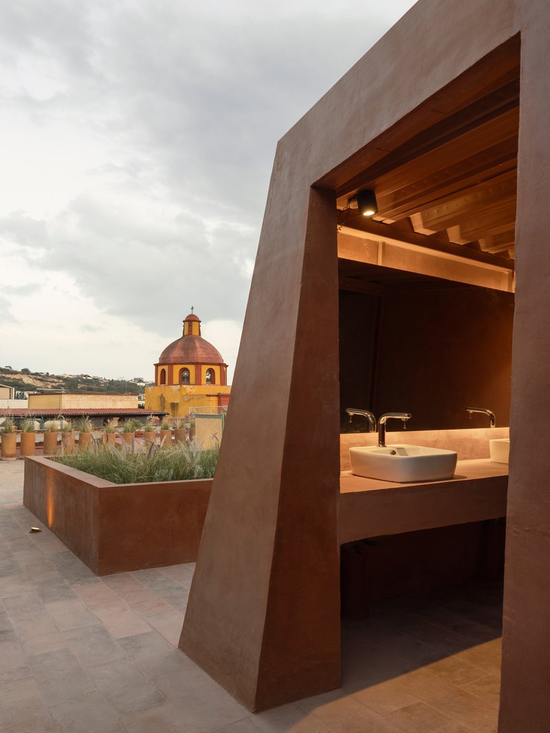 Rooftop terrace with weathered steel vanity niche and planter box at dusk, with a distant church dome