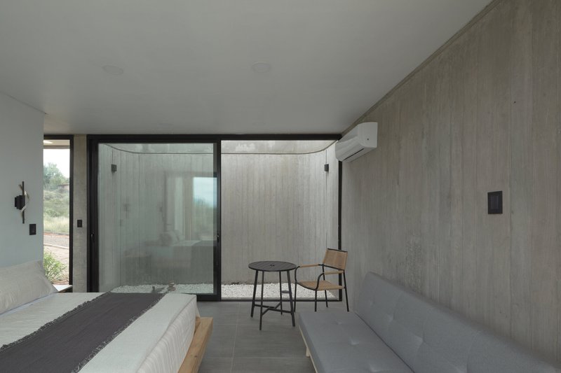 Bedroom interior with boardformed concrete walls and full-height glazing overlooking a private courtyard