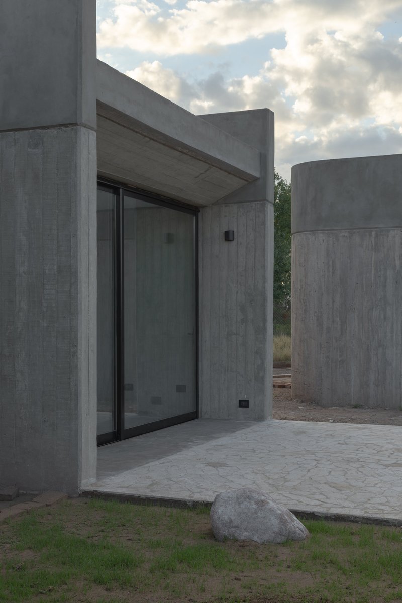 Recessed glass door beneath a concrete canopy flanked by cylindrical concrete volumes