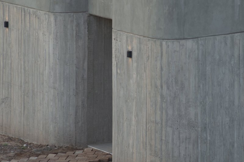 Close-up of curved board-formed concrete walls meeting at angular corners in flat light