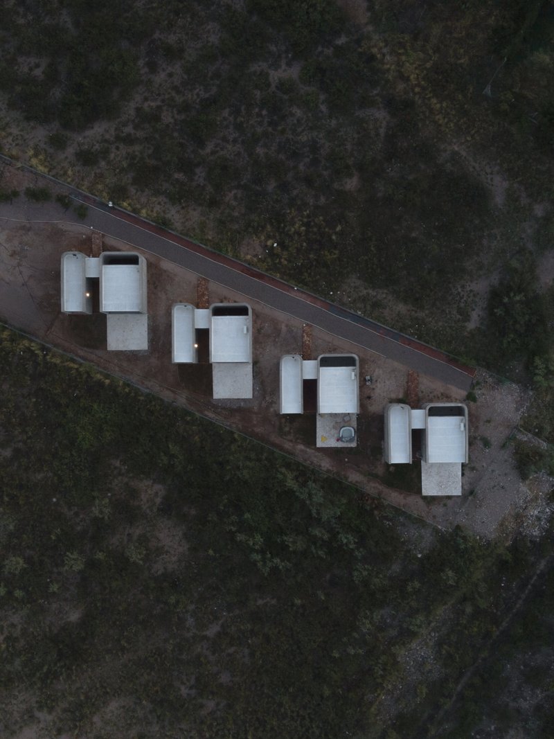 Aerial view of four white rectangular housing units aligned along a roadway in scrubland at dusk
