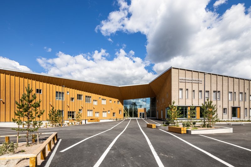 Entry facade with sweeping timber cladding and beige brick volume across a fresh-striped parking lot