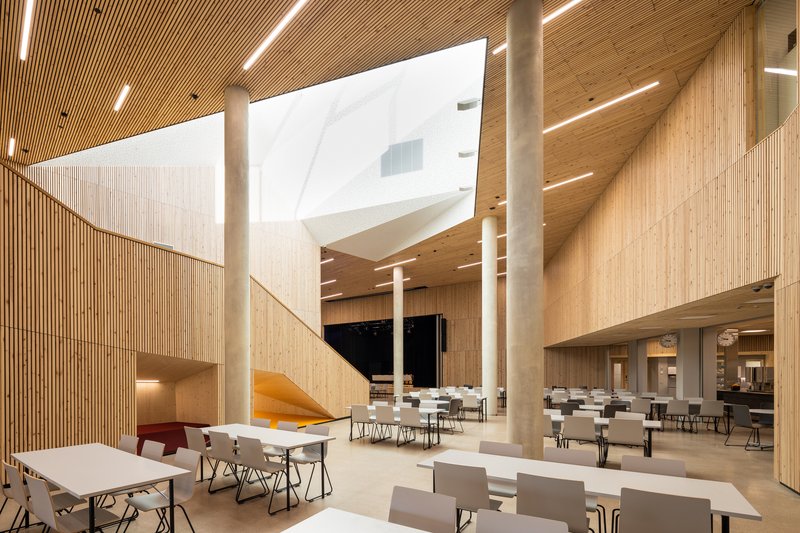 Double-height dining hall with timber columns, slat-clad walls, skylights and white tables throughout