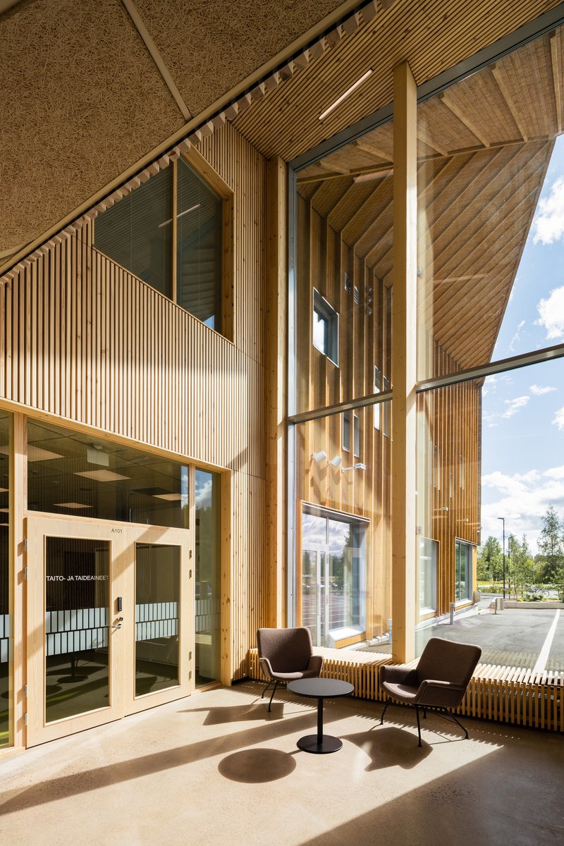 Double-height glazed entry space with vertical timber slat cladding and two armchairs casting shadows on polished concrete