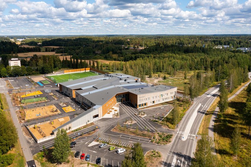 Aerial view of the campus with sports fields and surrounding forest under a cloudy sky