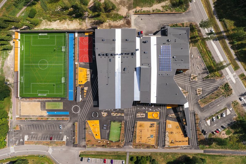 Top-down drone view showing the roofscape with sports courts and colorful play areas below