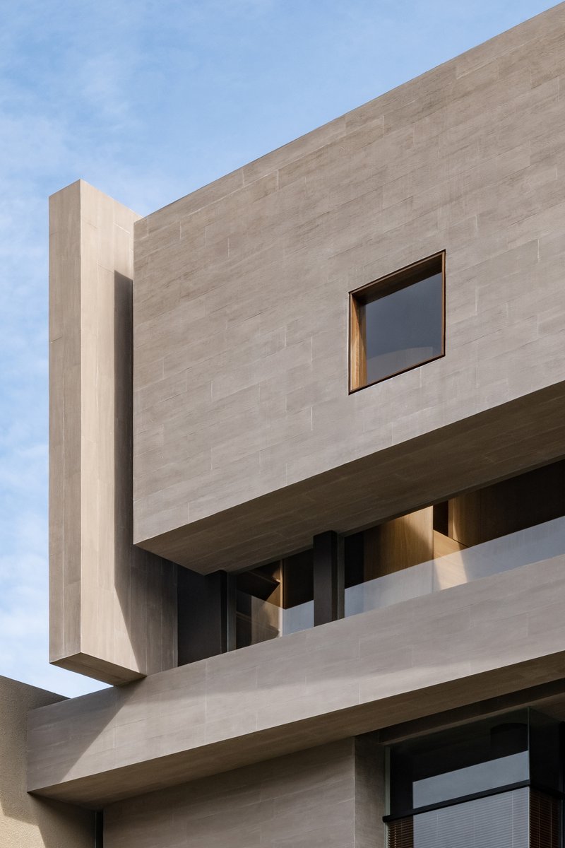 Corner detail of cantilevered concrete volume with square window and timber-lined soffit below
