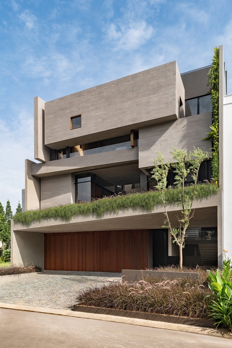 Street facade with stacked concrete volumes, planted terraces and timber garage door under blue sky