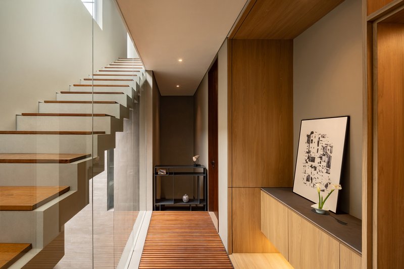 Entry hallway with cantilevered timber staircase and slatted mat leading to timber storage joinery