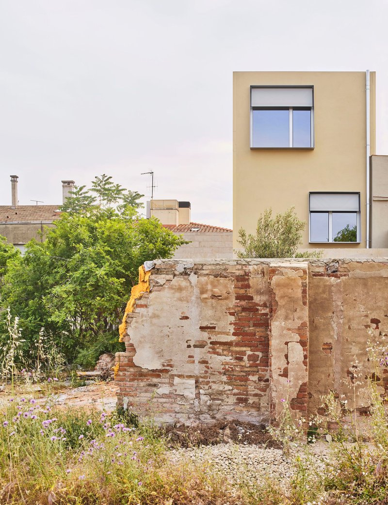 Weathered brick ruin wall with wild grasses in front of a pale yellow volume with stacked windows