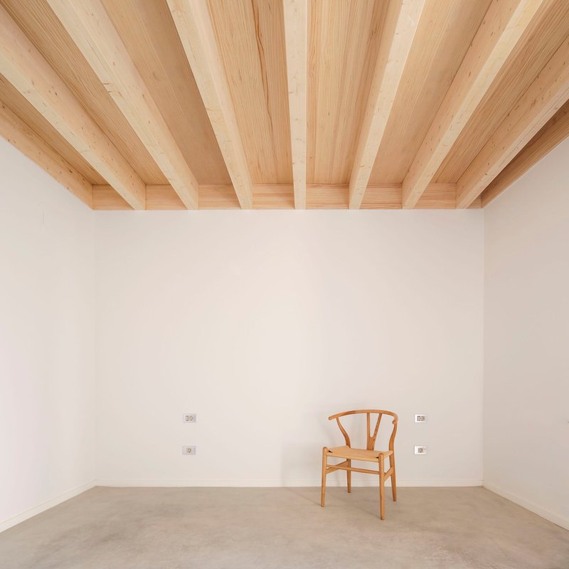 Interior corner with exposed timber beam ceiling and a single wooden chair on polished concrete floor