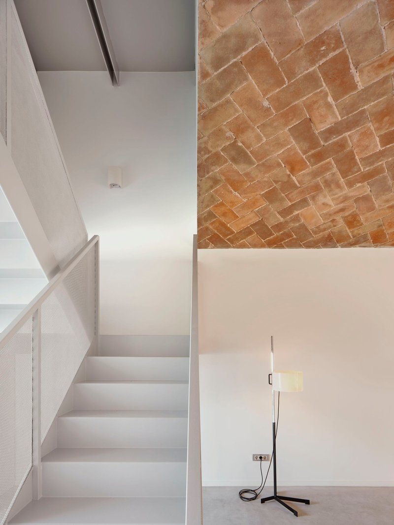 Stairwell with perforated metal balustrade where white plaster ceiling meets herringbone brick vault