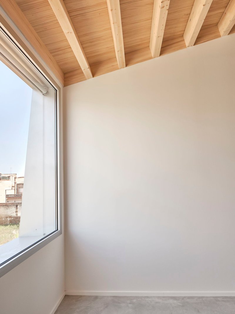 Corner room with exposed timber beams and a tall window overlooking rooftops under overcast sky