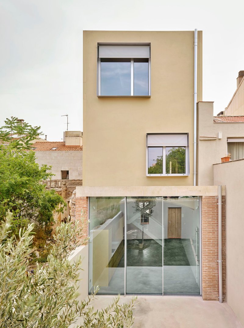 Street view of cream stucco facade with protruding windows and full-height glazed ground floor entry with brick surround