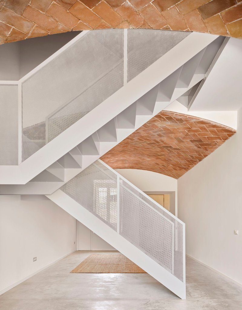 White metal stair with perforated balustrade ascending through space with terracotta vaulted ceiling patches