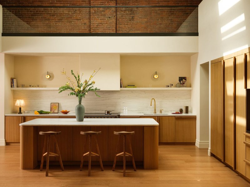 Kitchen island with walnut cabinetry and white countertop beneath exposed brick ceiling beams