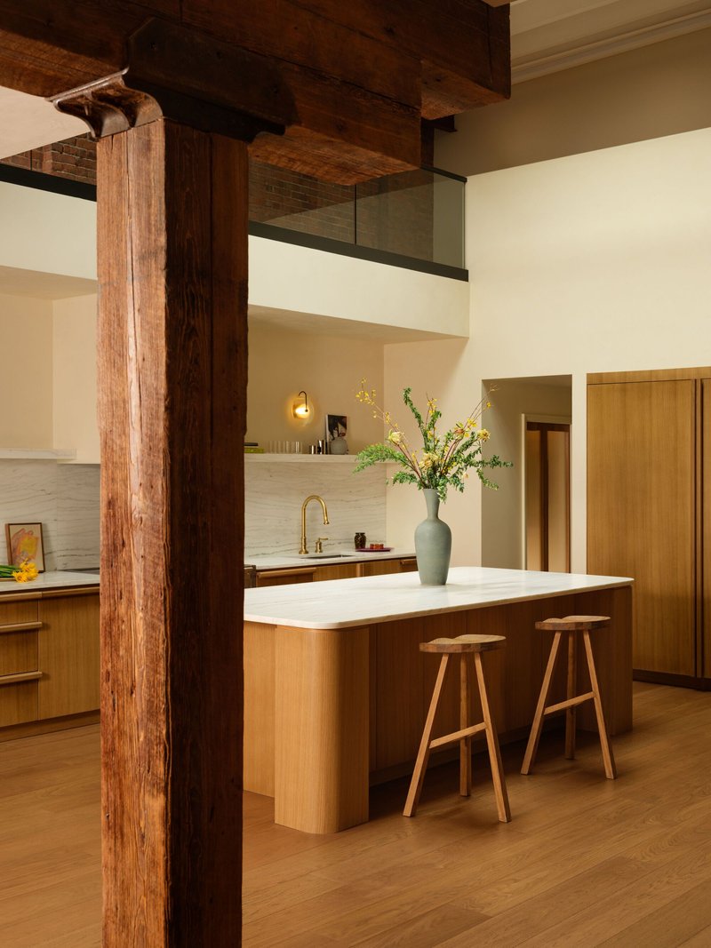 Open kitchen with timber island, wooden bar stools, and exposed ceiling beams framing a structural column