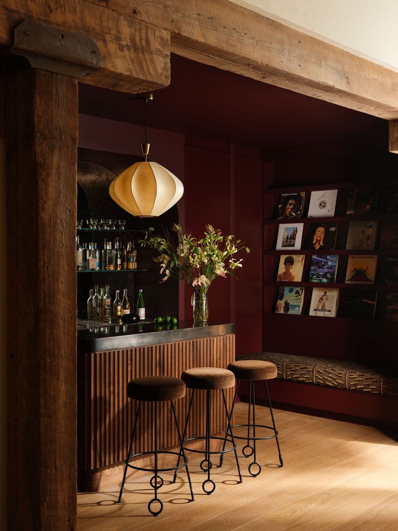 Bar nook with fluted timber front, burgundy walls, record display, and pendant light under timber beam