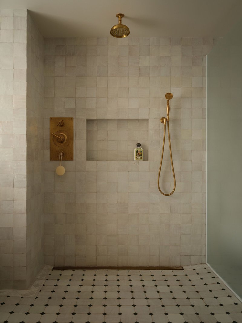 Tiled shower enclosure with brass fixtures and recessed niche on floor with octagonal mosaic pattern