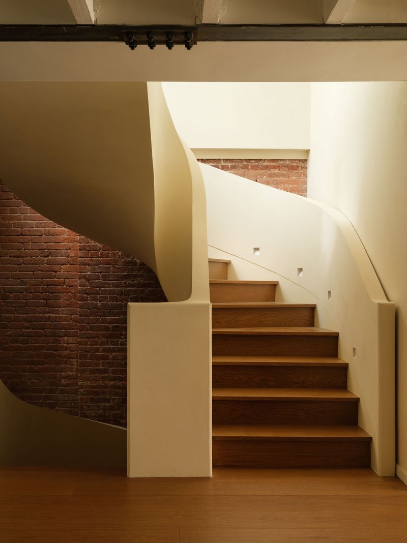 Curving timber staircase with sculptural cream-colored balustrade against an exposed brick wall