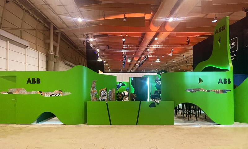 Bright green undulating exhibition walls with cutout openings under an exposed industrial ceiling