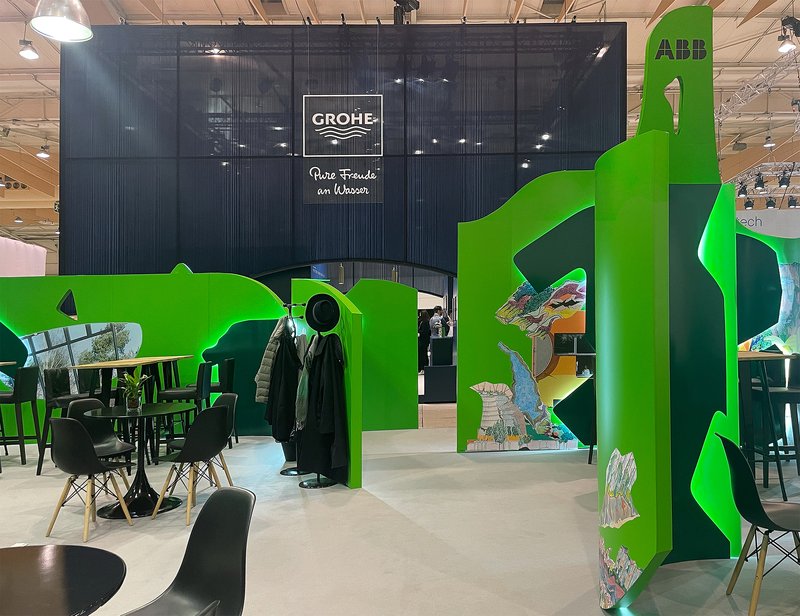 Exhibition booth with flowing green walls and cutout windows framing seating areas within