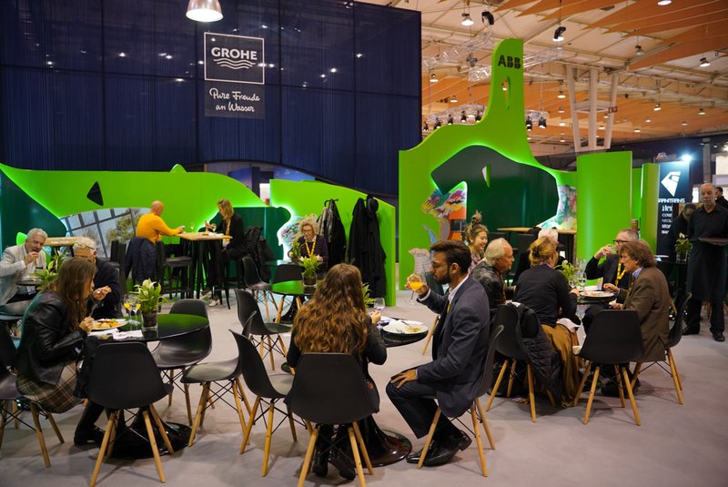 Seating area with round tables and chairs inside a lounge space defined by bright green curving walls