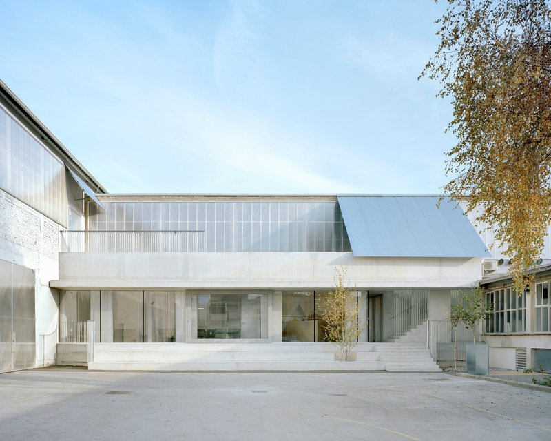 White concrete and translucent polycarbonate facade with cantilevered upper floor and young tree in courtyard