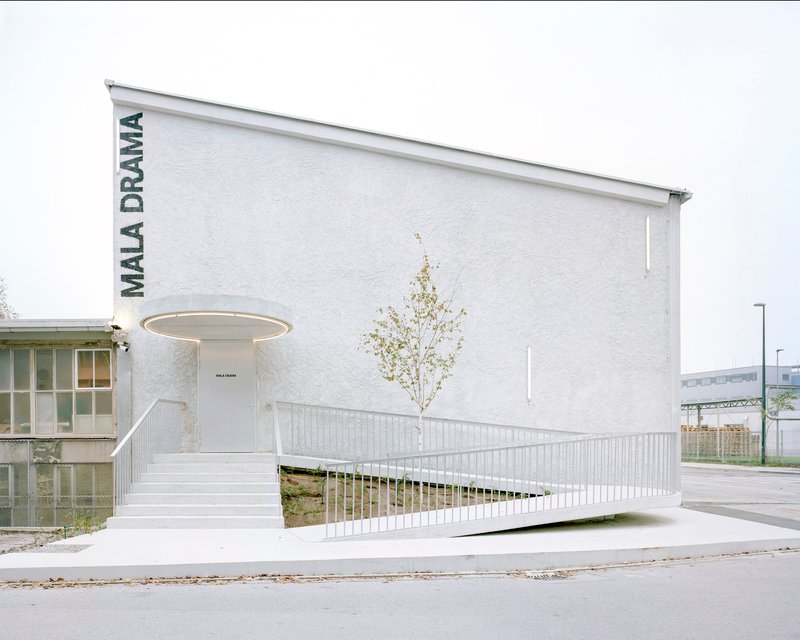 White rendered entrance facade with elevated walkway, circular canopy ring and single leafless sapling