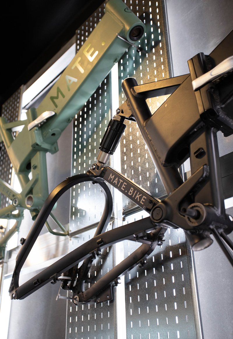 Close-up of folding bicycle frames suspended by chains against a perforated metal wall with backlighting