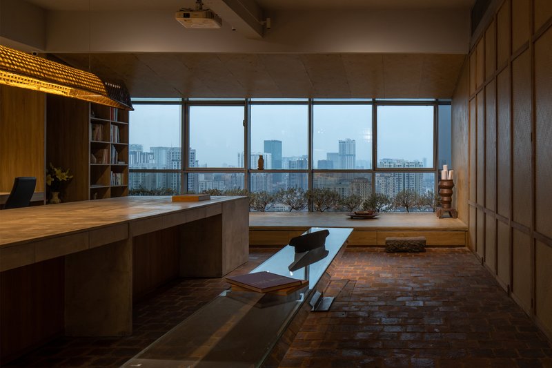 Interior workspace with timber desk and brick floor facing floor-to-ceiling windows overlooking the cityscape at dusk