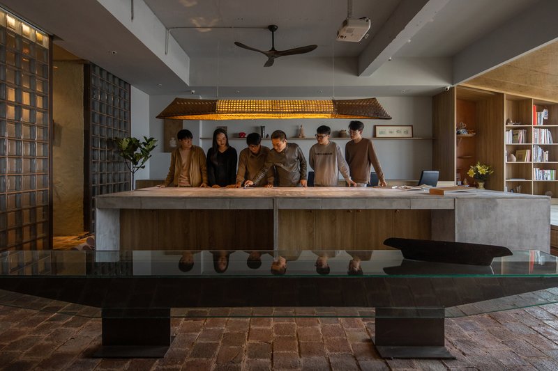 Interior workspace with staff gathered around a concrete counter beneath a woven timber pendant light