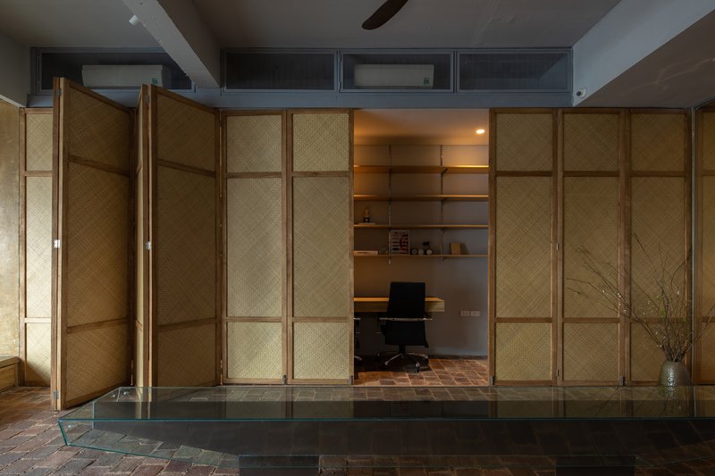 Folding woven bamboo screen panels opening to reveal a private office alcove with brick floor