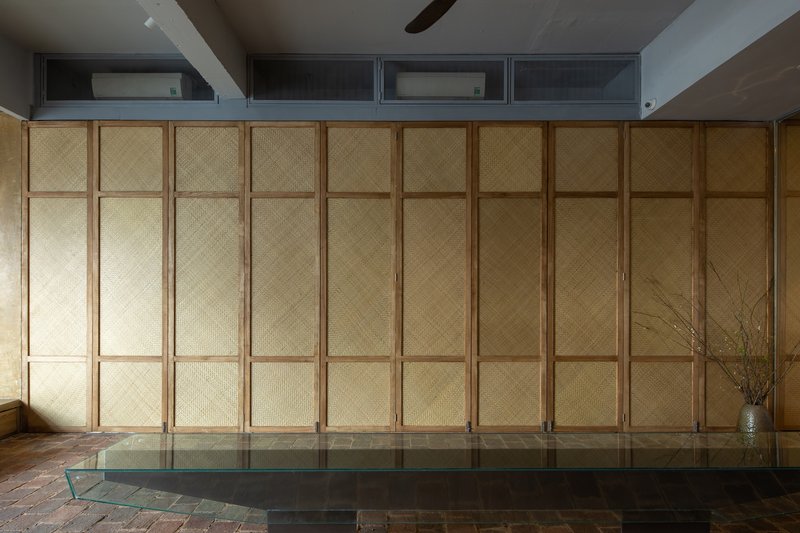 Closed woven timber partition wall with raised platform and terracotta brick floor at base
