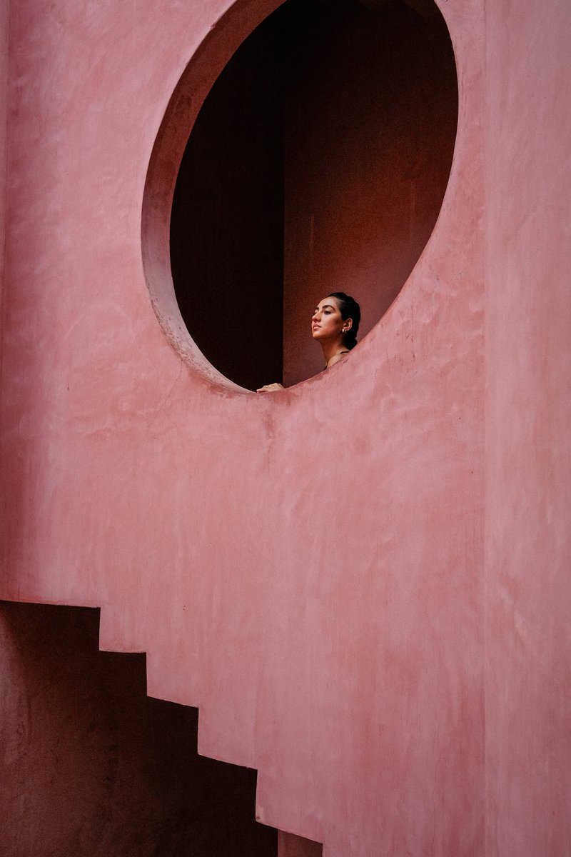 Oval opening in a pink plastered wall with a figure looking out and a staircase below