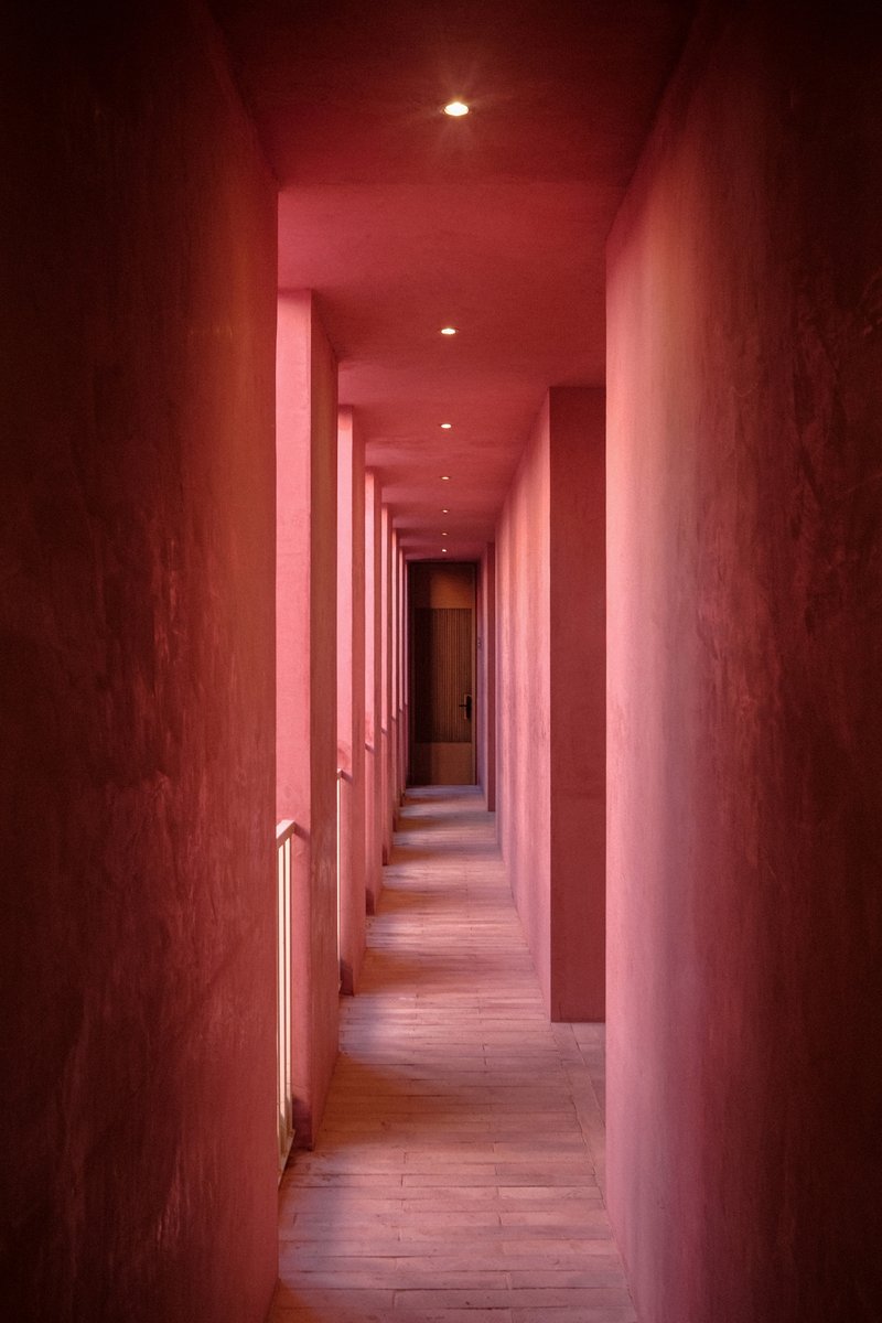 Long corridor with pink plaster walls, recessed ceiling lights and timber flooring stretching into the distance