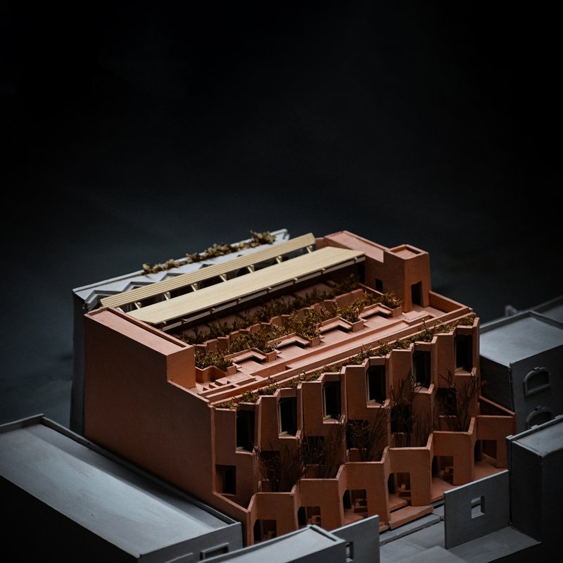 Physical model showing terraced copper facades with planted trees along stepped massing in dramatic lighting