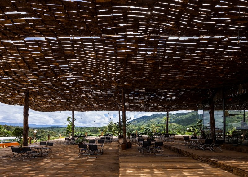 Dappled light filtering through the woven bamboo ceiling onto the timber deck and seating below