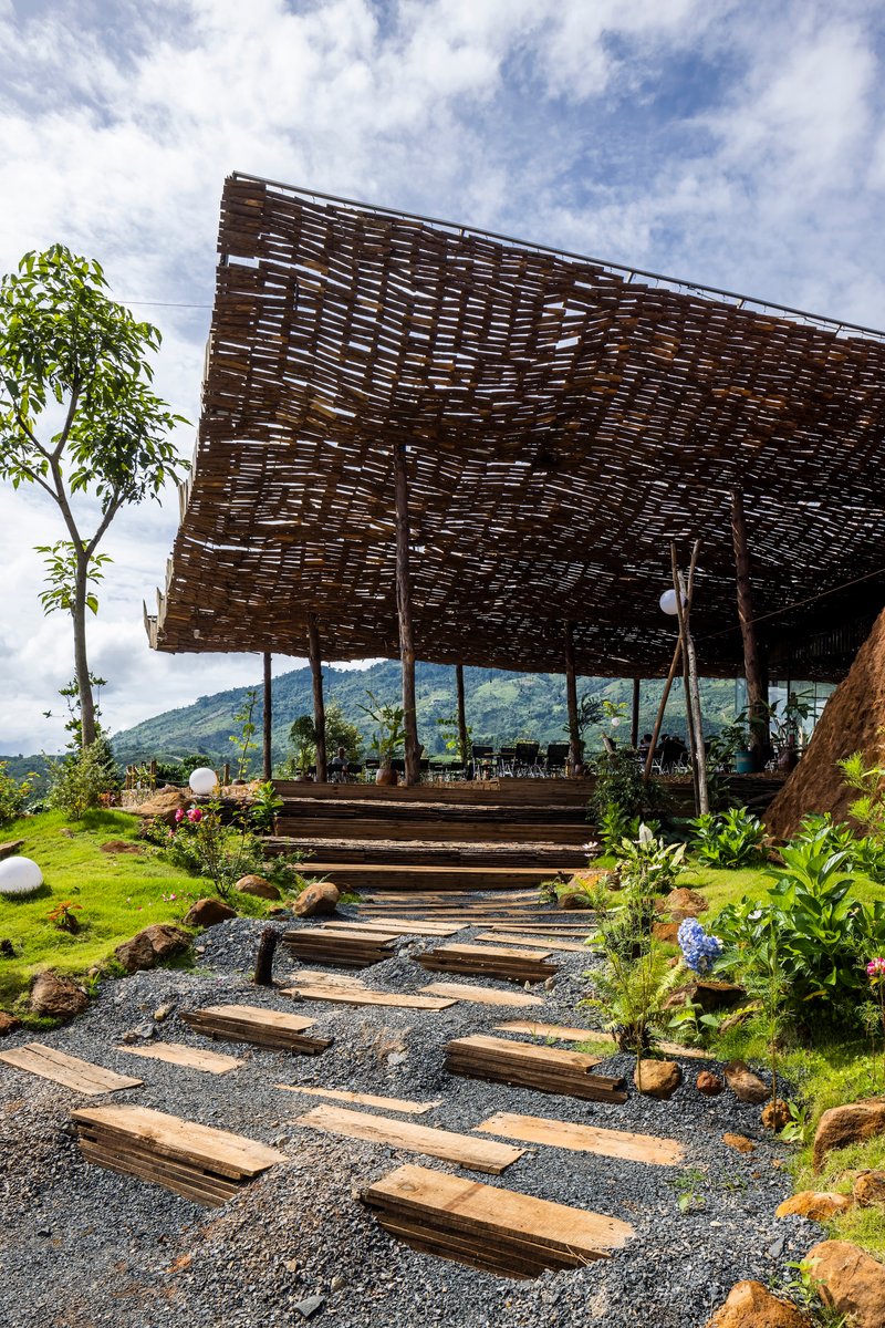 Timber plank pathway on gravel leading toward the woven screen pavilion with hillside landscape beyond