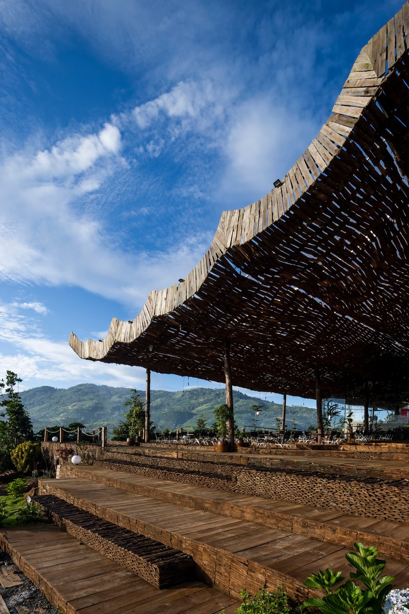 Stepped timber platforms leading up to the woven bamboo roof structure against distant green peaks