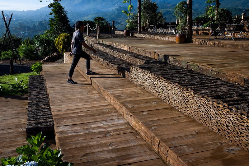 Visitor crossing wide timber deck platforms bordered by woven bamboo retaining walls in morning light
